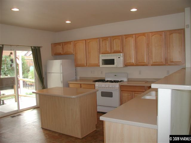 1214 Secluded Circle Reno, NV 89509 - Photo 4 of 9 a kitchen with kitchen island a stove a sink a refrigerator white cabinets and wooden floor