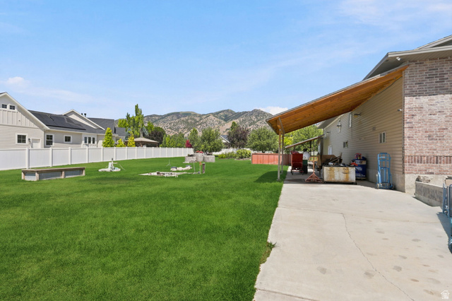 580 North 300 East Logan, UT 84321 - Photo 59 of 74 Expansive grassy yard with mountain backdrop, featuring a white privacy fence, concrete patio, and a covered wood-beam awning