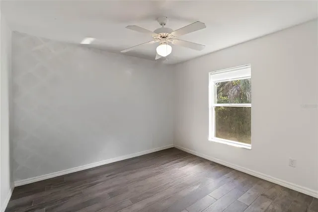 an empty room with wooden floor chandelier fan and windows