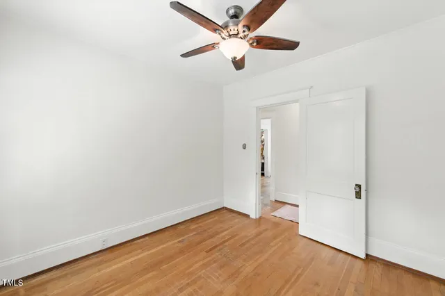 an empty room with wooden floor ceiling fan and window