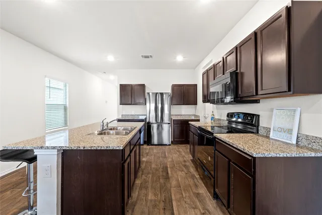 a large kitchen with granite countertop lots of counter top space a sink and stainless steel appliances