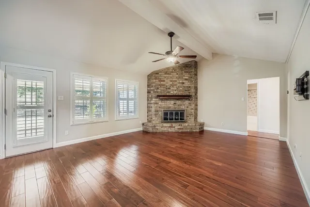 a view of an empty room with wooden floor fireplace and a window