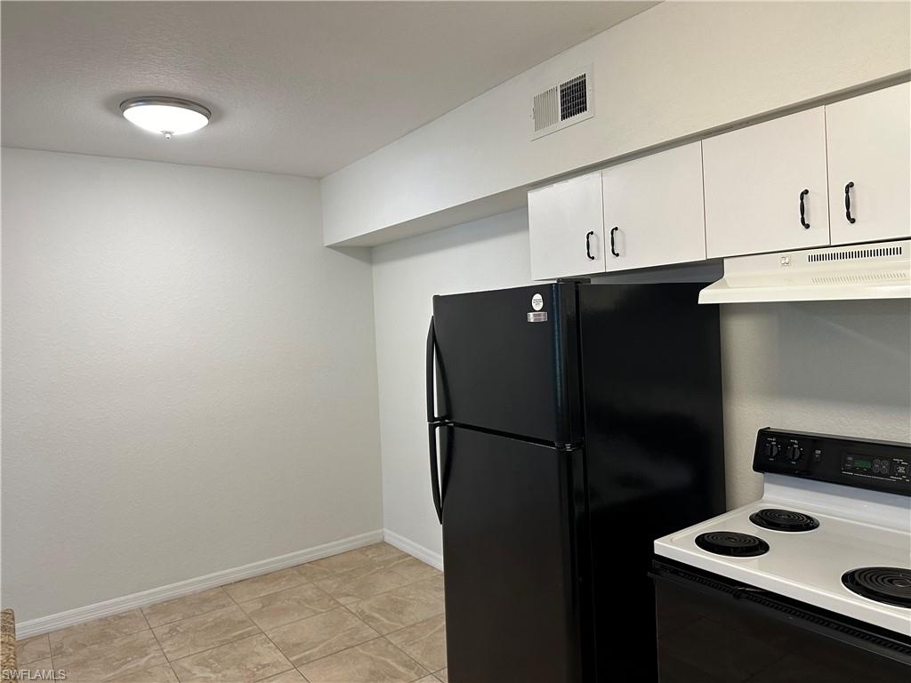 27103 Matheson Avenue, Unit 103 Bonita Springs, FL 34135 - Photo 17 of 29 Kitchen with white cabinets, white range with electric stovetop, light tile patterned flooring, and black fridge