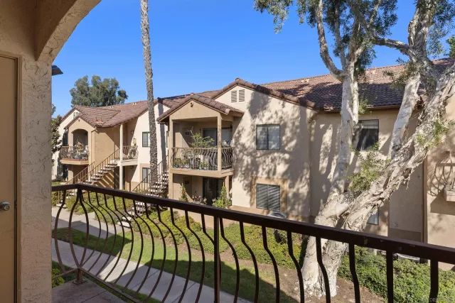 a view of a white house with a large tree and wooden fence