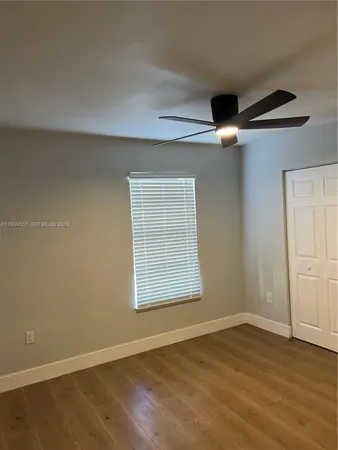 an empty room with wooden floor chandelier fan and windows