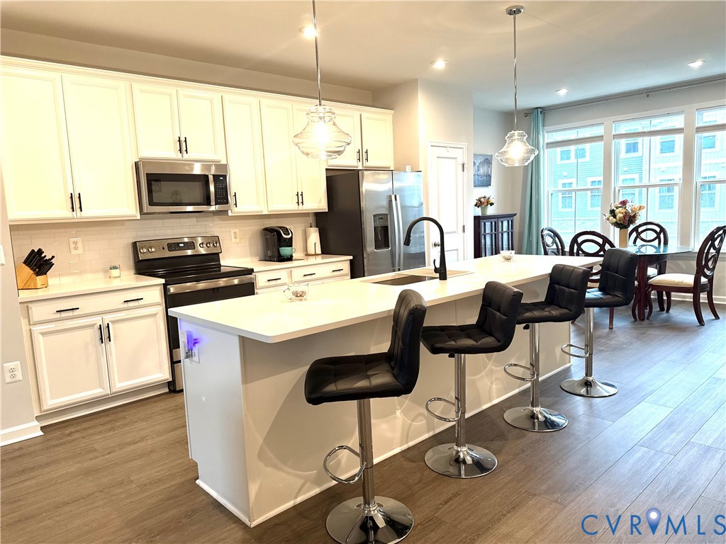 a kitchen with stainless steel appliances a stove a sink a microwave a refrigerator a dining table and chairs with wooden floor