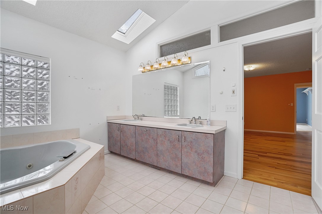 1094 San Raphael Drive Akron, OH 44333 - Photo 31 of 50 Bathroom featuring a skylight, light tile patterned flooring, double vanity, a tub with jets, and vaulted ceiling