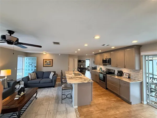 a living room with stainless steel appliances kitchen island granite countertop a couch and a view of kitchen next to a window