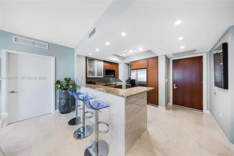 a kitchen with stainless steel appliances kitchen island granite countertop a refrigerator a stove a sink a microwave a dining table and chairs with wooden floor