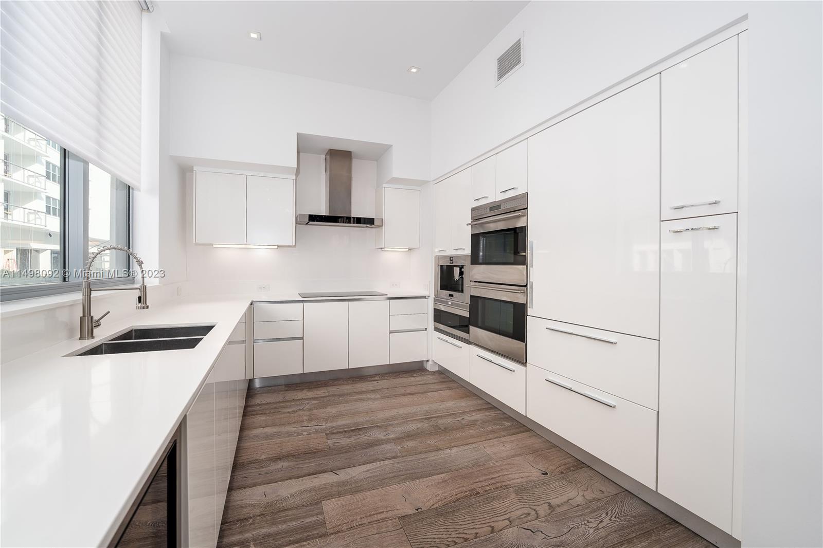 9501 Collins Avenue, Unit 1 Surfside, FL 33154 - Photo 6 of 35 a kitchen with stainless steel appliances granite countertop a sink and white cabinets with wooden floor