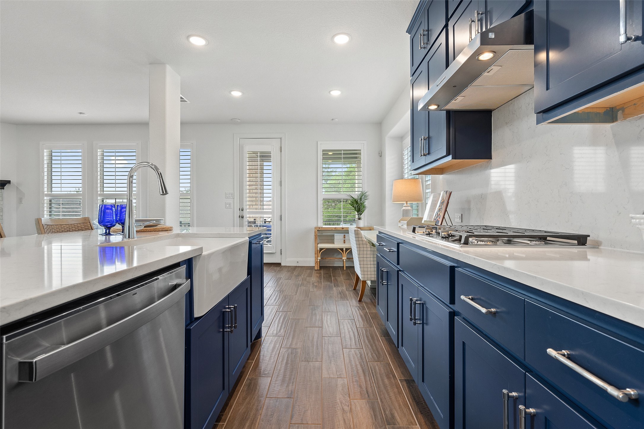 604 Pecan Bottom Trail Georgetown, TX 78628 - Photo 11 of 40 Kitchen featuring blue cabinetry, appliances with stainless steel finishes, light stone countertops, dark wood finished floors, and under cabinet range hood
