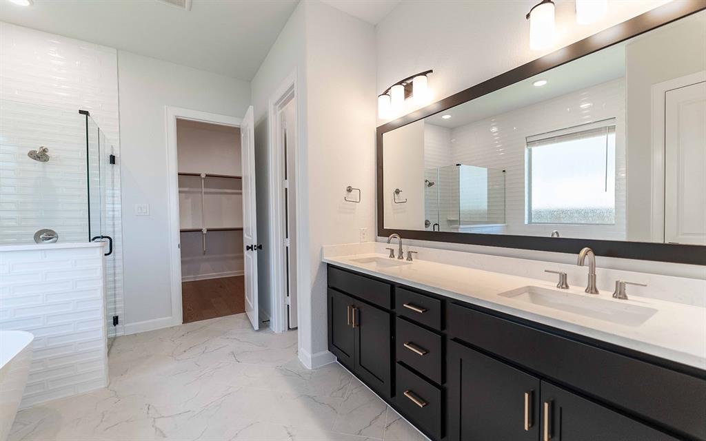 2008 Casting Ridge Mesquite, TX 75181 - Photo 15 of 24 Spacious bathroom featuring a double vanity with dark cabinetry and light countertops, a large framed mirror, and a glass-enclosed shower with white subway tile
