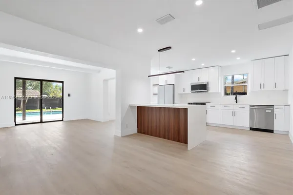 a view of a kitchen with stainless steel appliances granite countertop a stove top oven a sink dishwasher and white cabinets with wooden floor
