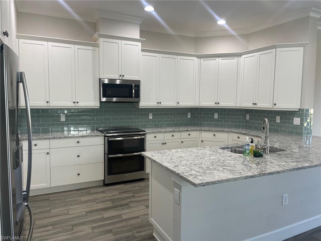 5685 Highbourne Drive Naples, FL 34113 - Photo 17 of 26 a kitchen with stainless steel appliances granite countertop a stove and white cabinets