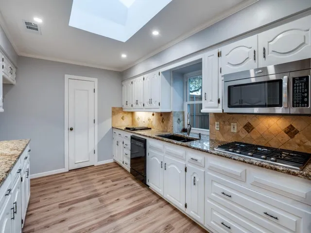 a kitchen with granite countertop a stove top oven a sink dishwasher a dining table and chairs with wooden floor