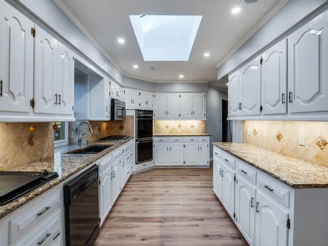 a large kitchen with stainless steel appliances granite countertop a stove top oven a sink dishwasher and a refrigerator with wooden cabinets