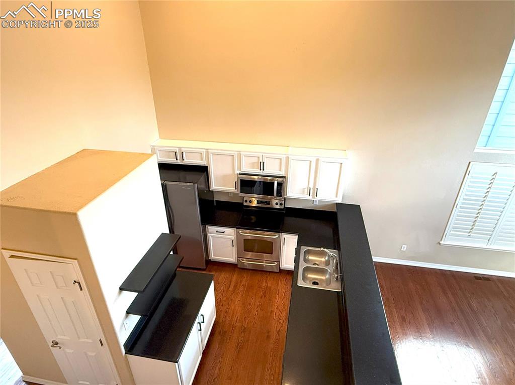 7313 Owings Point Peyton, CO 80831 - Photo 9 of 47 Kitchen featuring white cabinetry, appliances with stainless steel finishes, dark wood-style flooring, dark countertops, and a towering ceiling