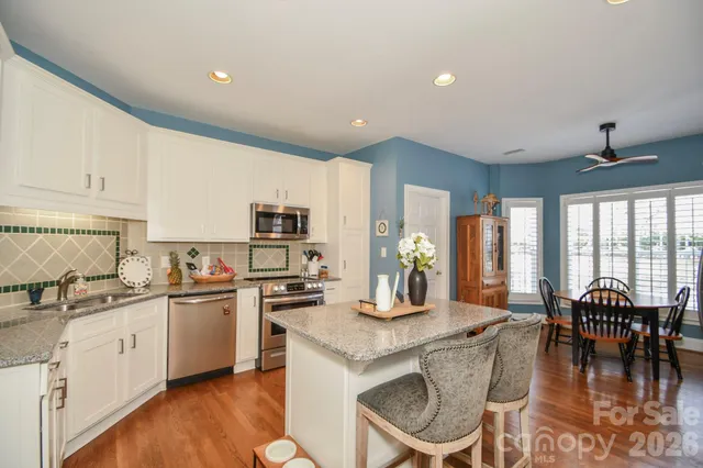 a kitchen with stainless steel appliances granite countertop a stove top oven a sink a dining table and chairs