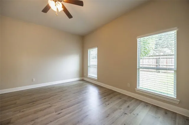 a view of an empty room with wooden floor and a ceiling fan