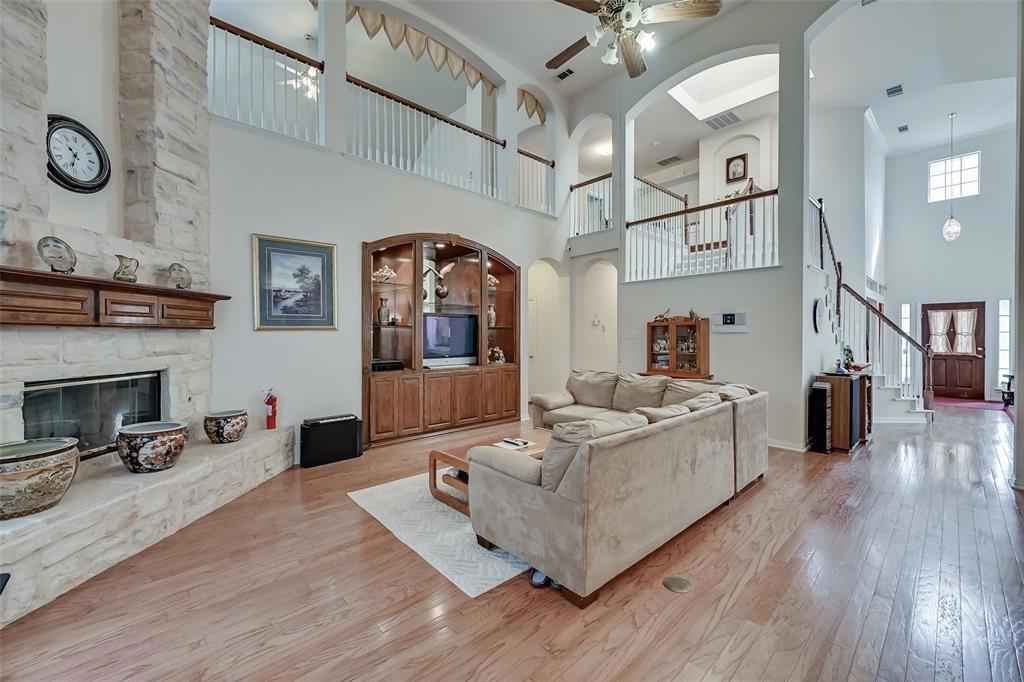 Living area featuring light wood-type flooring, arched walkways, a fireplace, a ceiling fan, and a high ceiling