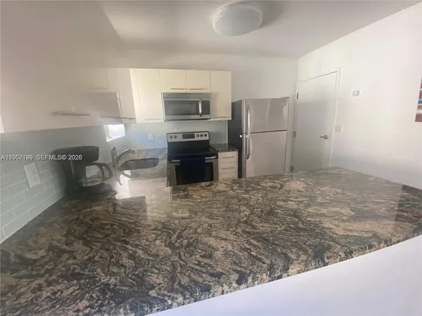 a kitchen with stainless steel appliances kitchen island granite countertop a refrigerator stove oven and white cabinets