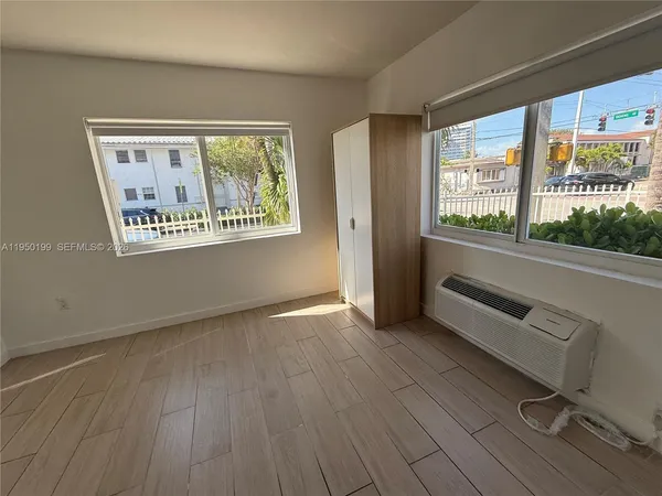 a view of an empty room with window and hardwood floor