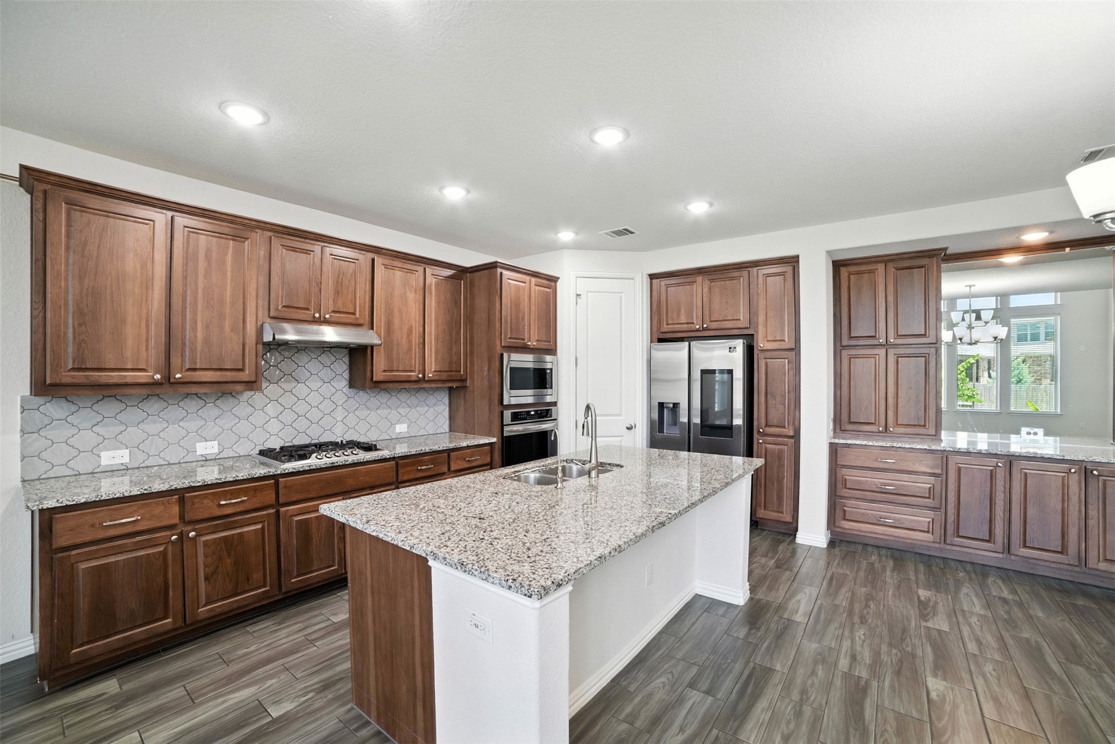 3054 Columbus Loop Round Rock, TX 78665 - Photo 10 of 40 Kitchen with appliances with stainless steel finishes, decorative backsplash, a chandelier, wood finish floors, and light stone counters
