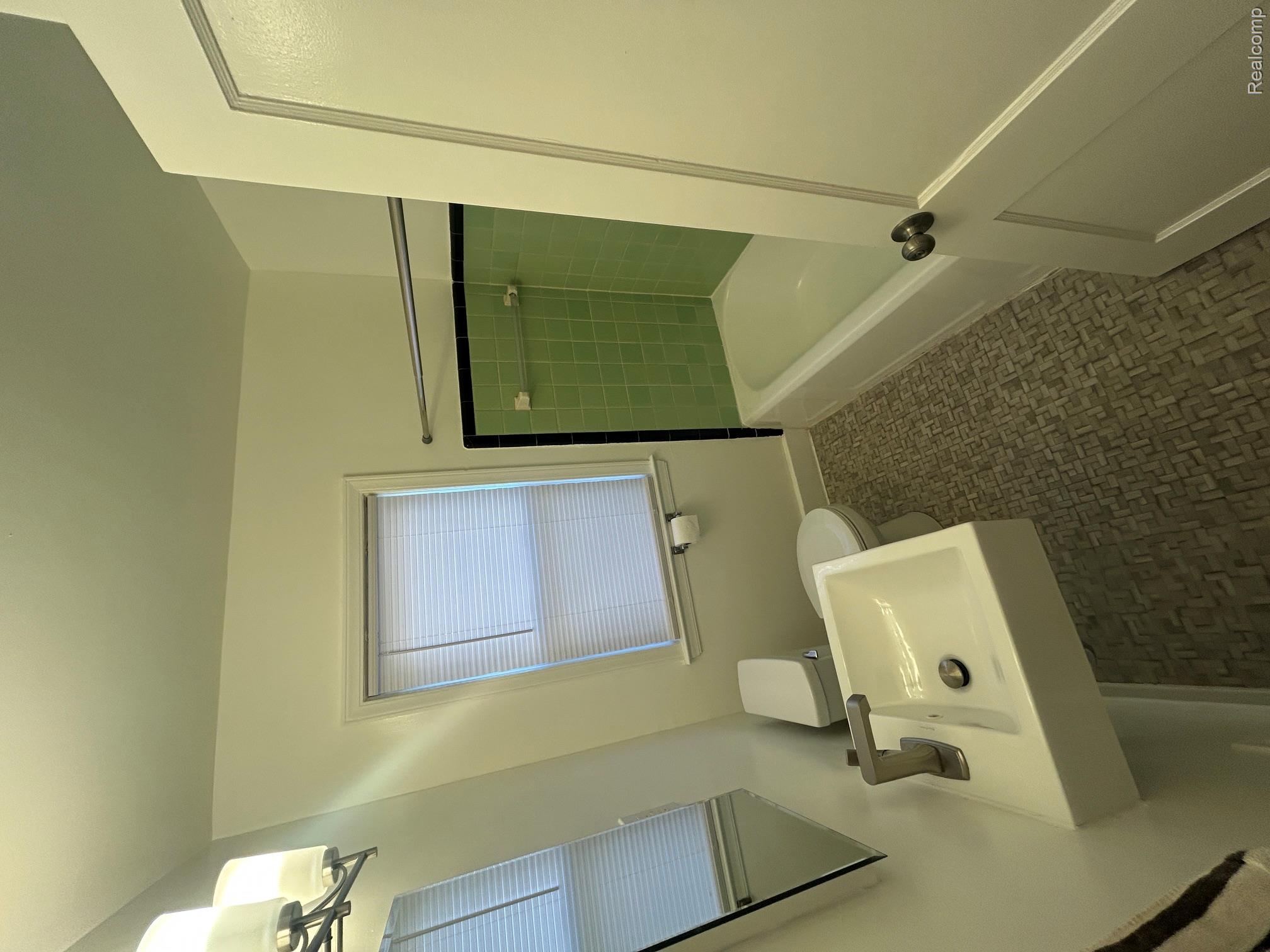 21970 Moross Road Grosse Pointe, MI 48236 - Photo 7 of 21 Bathroom featuring a wall-mounted sink with a modern faucet, a toilet, a window with blinds, a bathtub with green tile surround, and patterned floor tiling