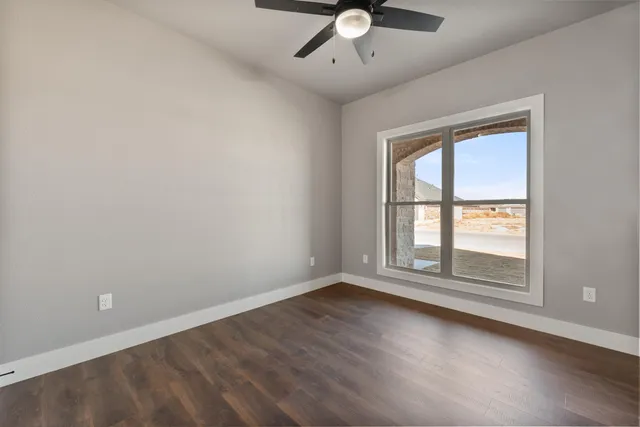 an empty room with wooden floor fan and windows