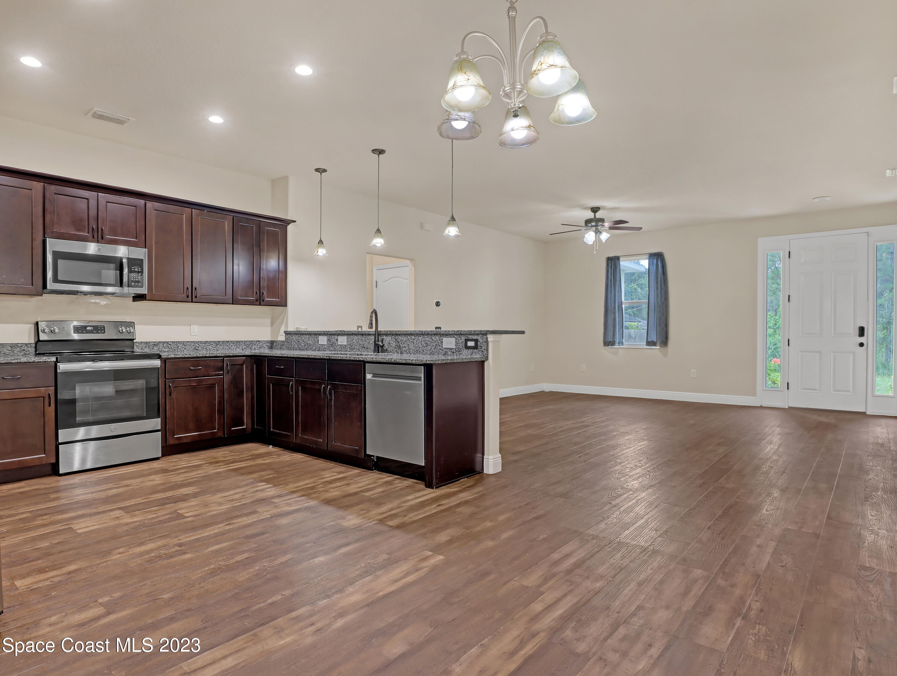 1310 Gaucho Road Southwest Palm Bay, FL 32908 - Photo 12 of 32 a large kitchen with stainless steel appliances granite countertop a stove a sink dishwasher a microwave oven with cabinets and wooden floor