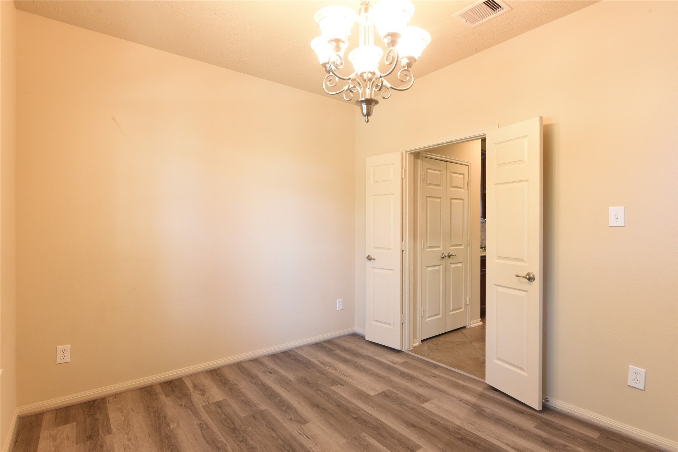 118 East Lasting Spring Circle Spring, TX 77389 - Photo 9 of 46 Bright room featuring Luxurious Vinyl Laminate flooring, neutral walls, and a stylish chandelier, with double doors leading to an adjacent Kitchen.