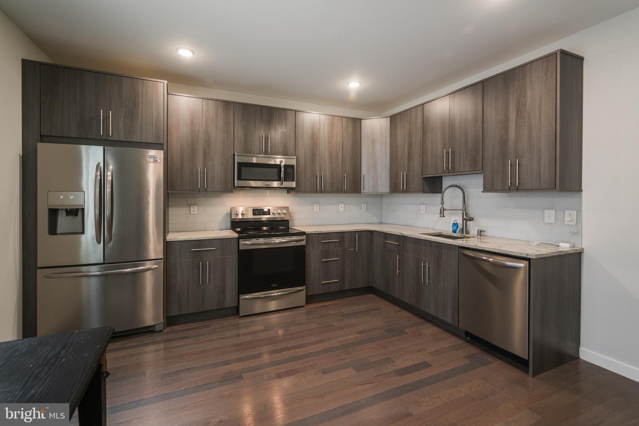 1524 North 8th Street, Unit 2 Philadelphia, PA 19122 - Photo 3 of 22 a kitchen with kitchen island granite countertop stainless steel appliances and wooden cabinets