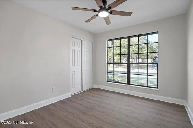 an empty room with wooden floor fan and windows