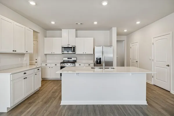 a large kitchen with stainless steel appliances granite countertop a stove a sink a refrigerator and white cabinets with wooden floor