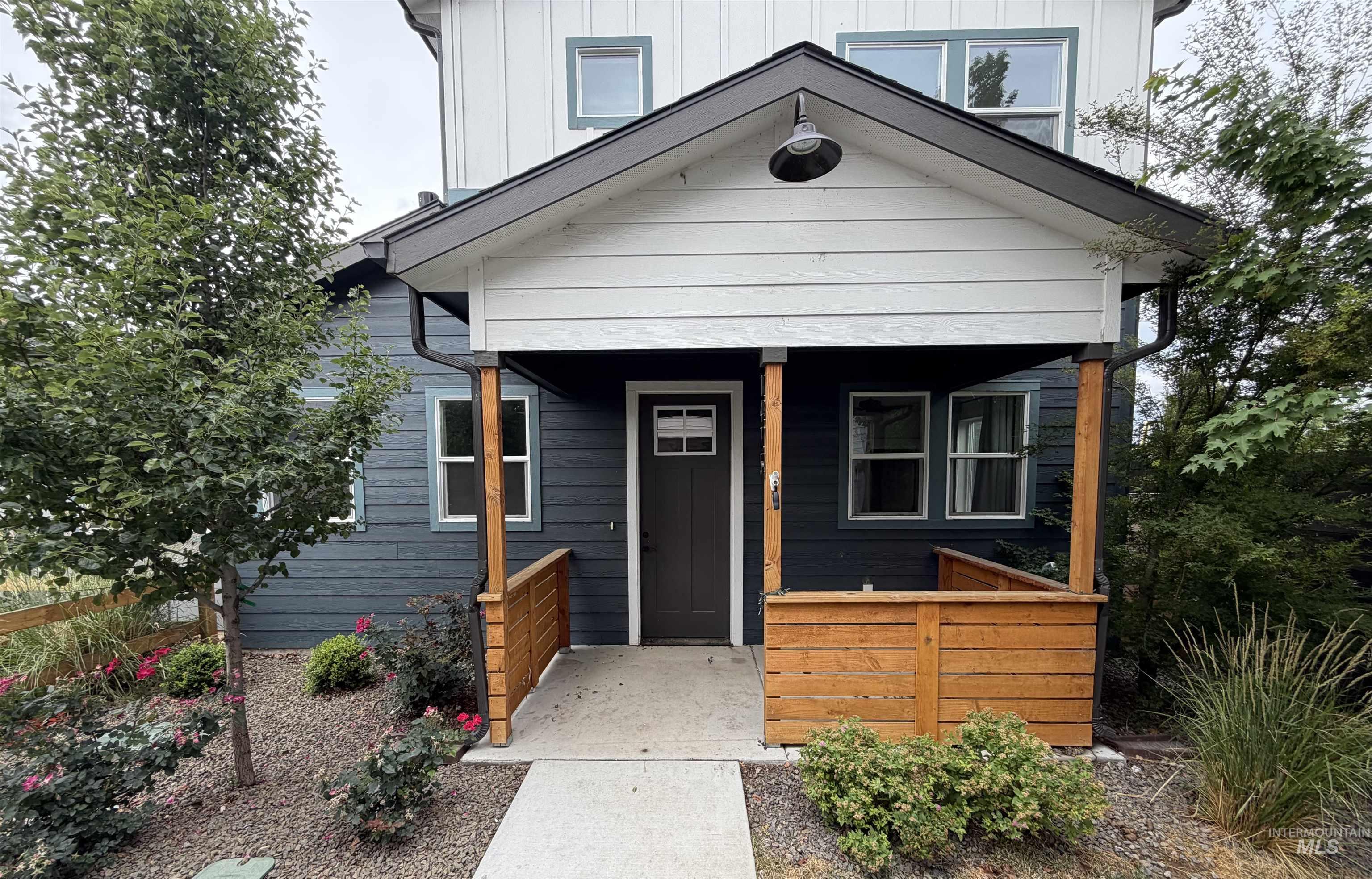 1475 North Bluffs Ridge Lane Boise, ID 83704 - Photo 1 of 13 Modern farmhouse exterior featuring dark blue horizontal siding, white board-and-batten siding, a covered porch with natural wood accents, and a landscaped front yard with decorative rock and plantings