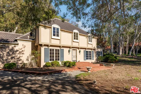 a view of a white house next to a yard with large trees