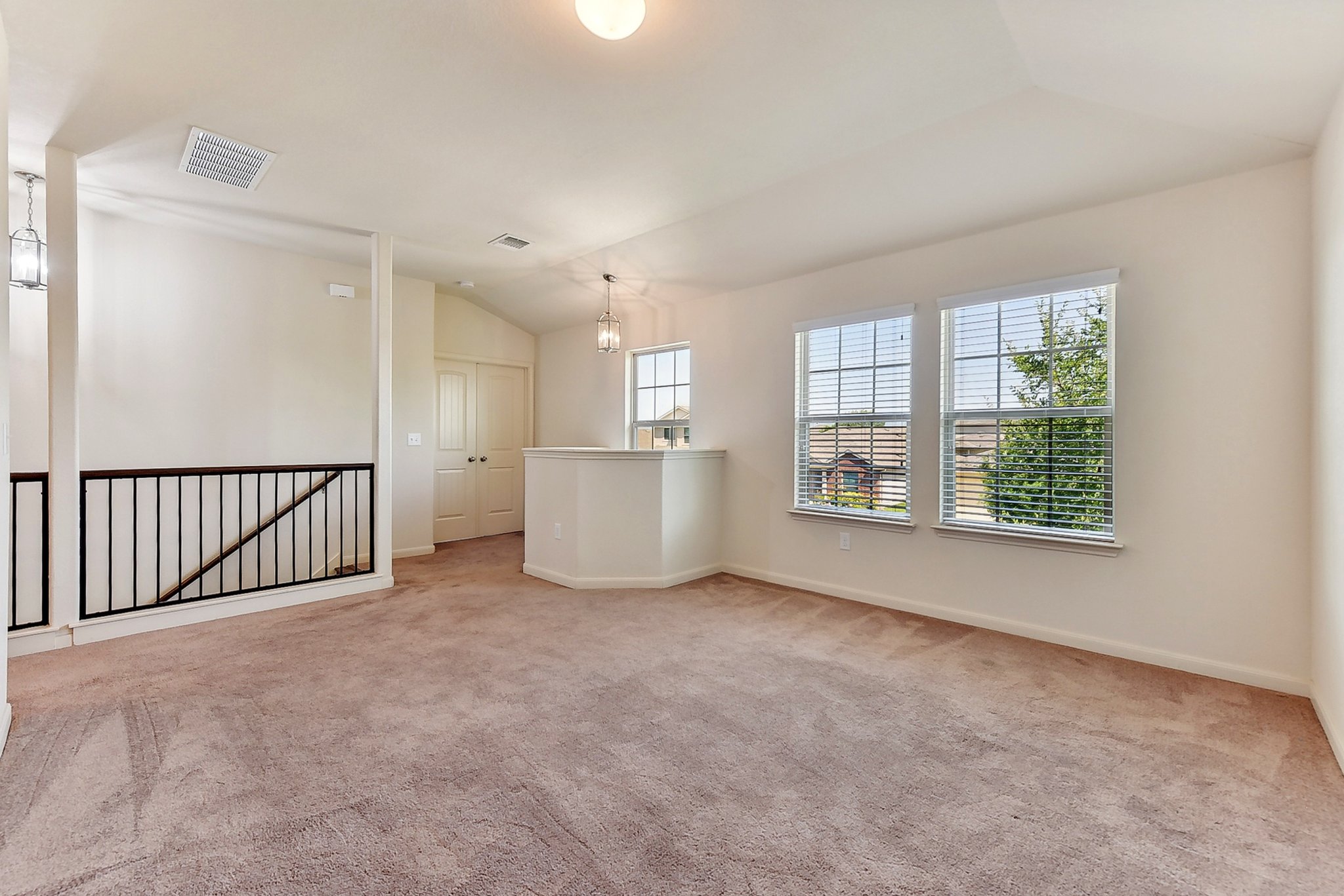 310 Potters Peak Way Georgetown, TX 78626 - Photo 19 of 21 Carpeted loft space with vaulted ceilings, two large windows with blinds, a black metal railing overlooking the floor below, and two pendant light fixtures
