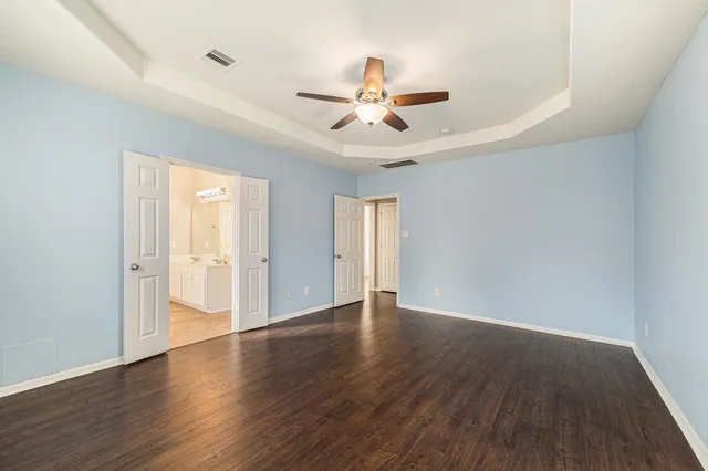 an empty room with wooden floor ceiling fan and windows