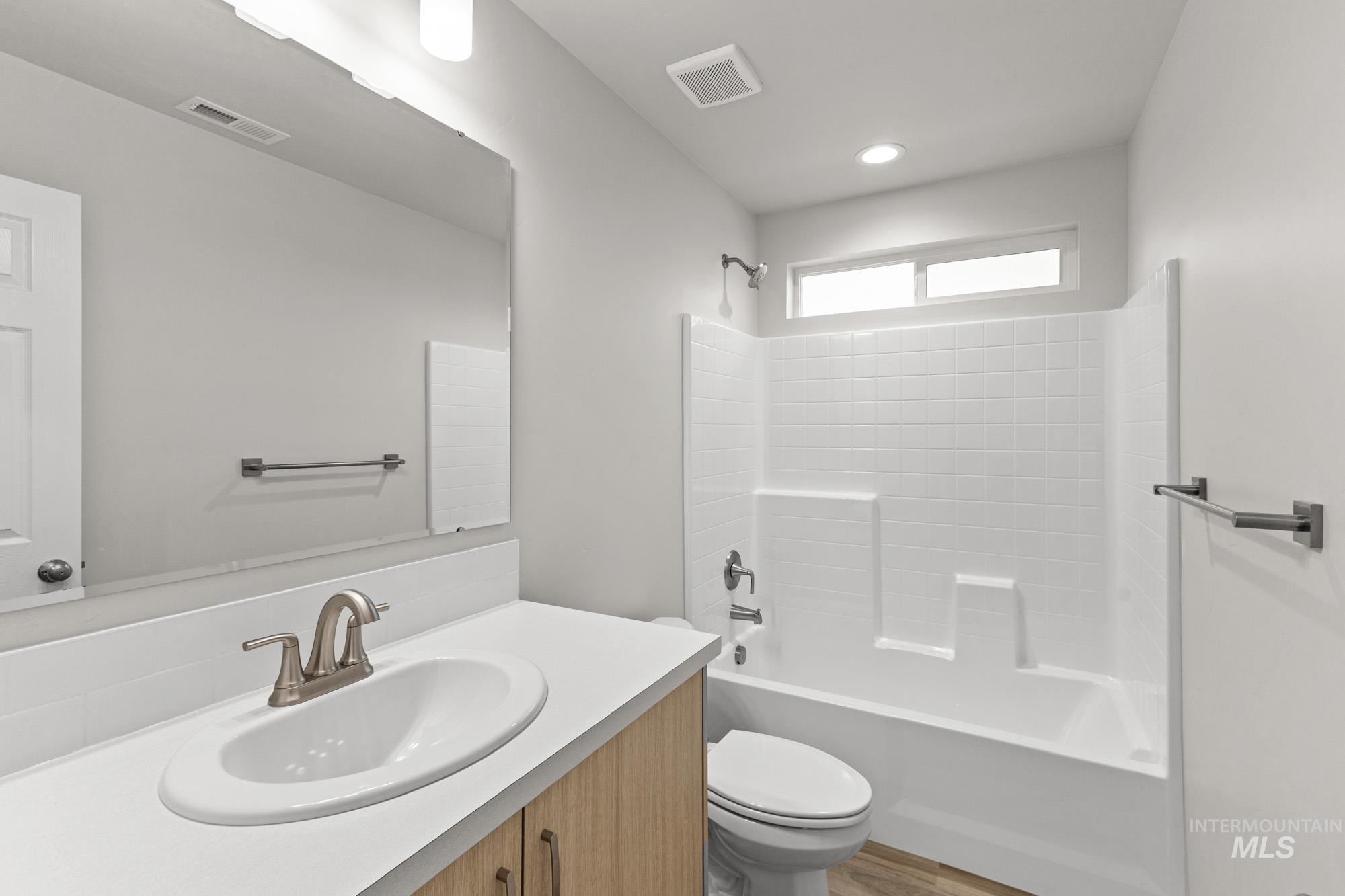 13307 Bank Street Caldwell, ID 83607 - Photo 16 of 20 Bathroom featuring a white bathtub with tile surround, wood-finish vanity, integrated sink, and brushed nickel fixtures