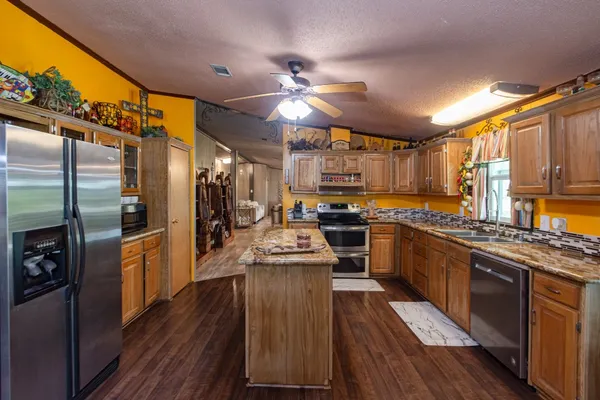 a kitchen with stainless steel appliances kitchen island granite countertop a stove refrigerator and cabinets