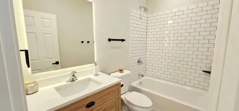 a bathroom with a granite countertop bathtub shower sink vanity mirror and toilet