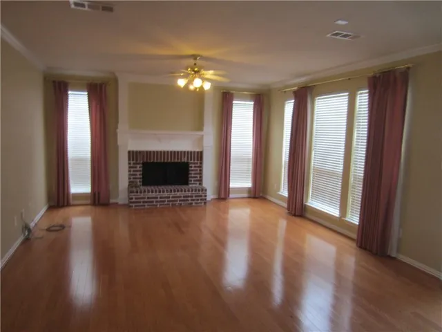 an empty room with wooden floor fireplace and windows