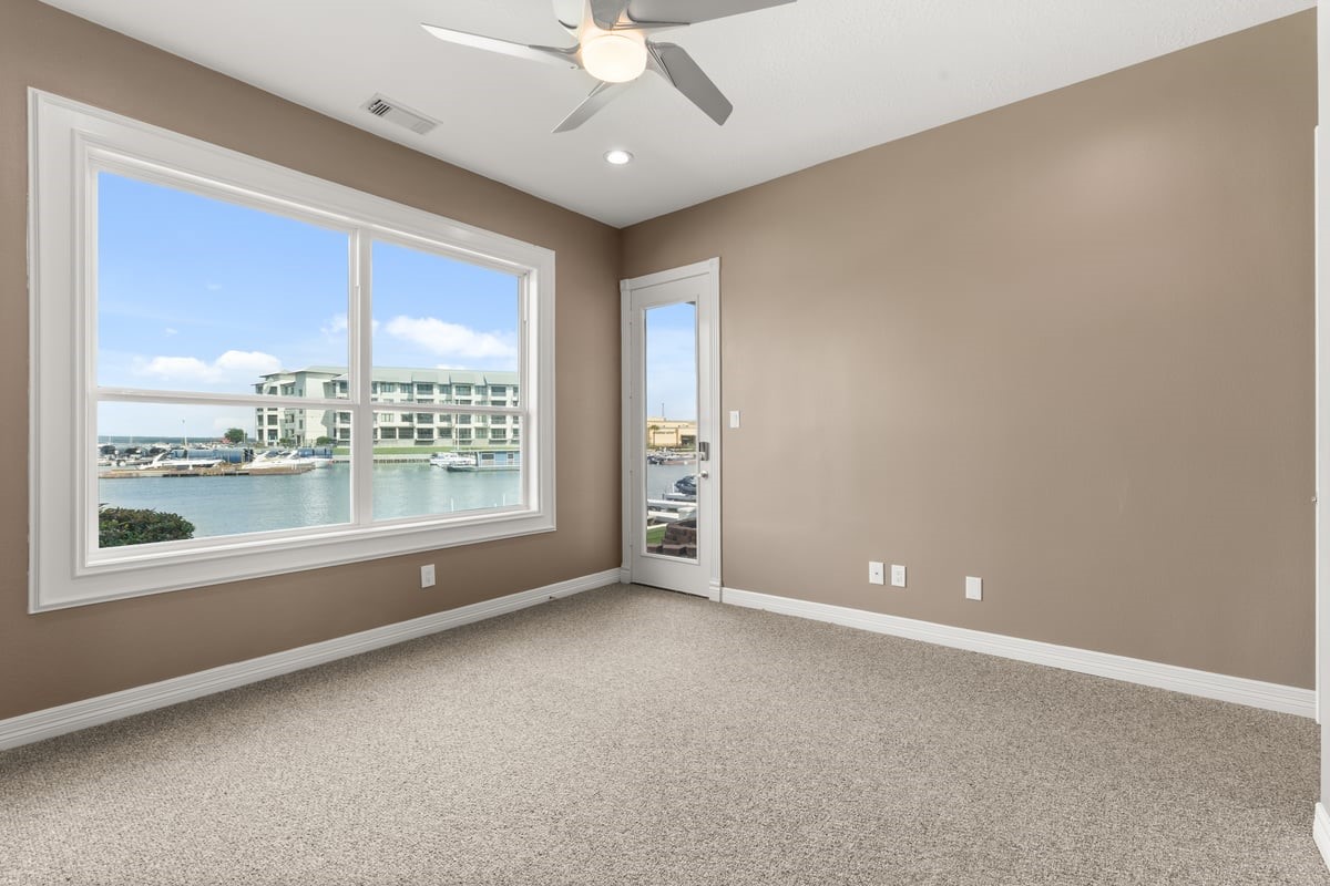 168 Lake Point Boulevard, Unit C102 Conroe, TX 77356 - Photo 15 of 35 This room features large windows with a stunning waterfront view, neutral walls, and carpeting. It includes a ceiling fan and a glass door leading outside, providing natural light and a serene atmosphere.
