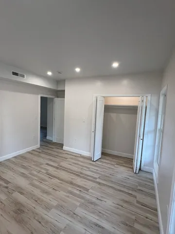 a view of an empty room with wooden floor and closet
