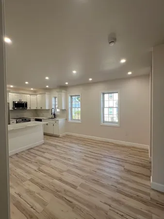 a view of an empty room with kitchen and window