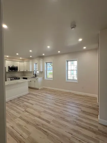a view of an empty room with kitchen and window