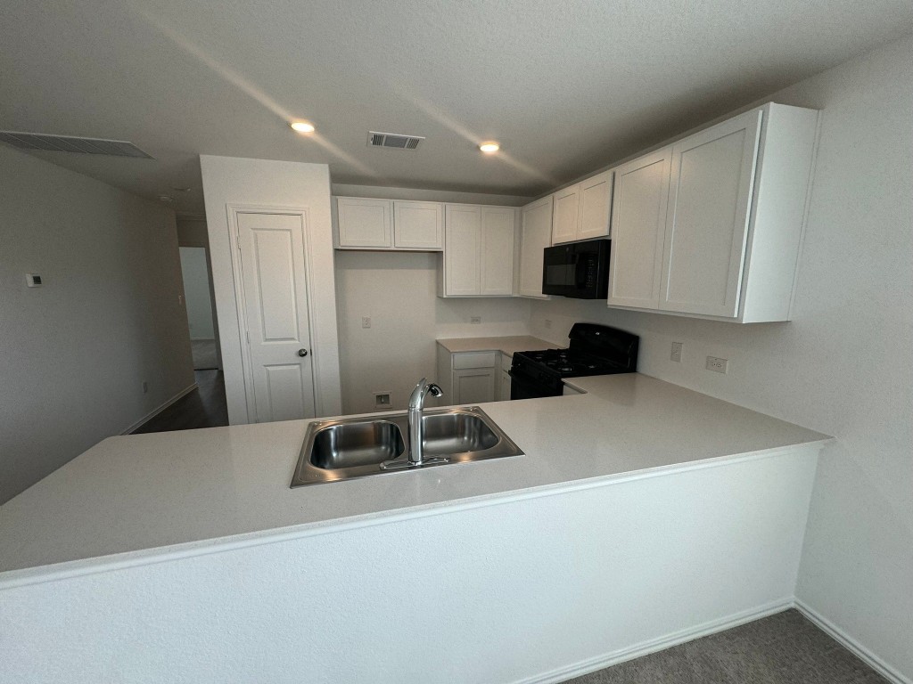 134 Avre Loop Kyle, TX 78640 - Photo 2 of 9 Kitchen with light countertops, black appliances, a peninsula, white cabinets, and recessed lighting
