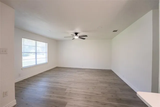 an empty room with wooden floor fan and windows