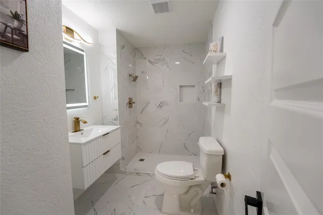 a bathroom with a granite countertop toilet a sink a mirror and shower