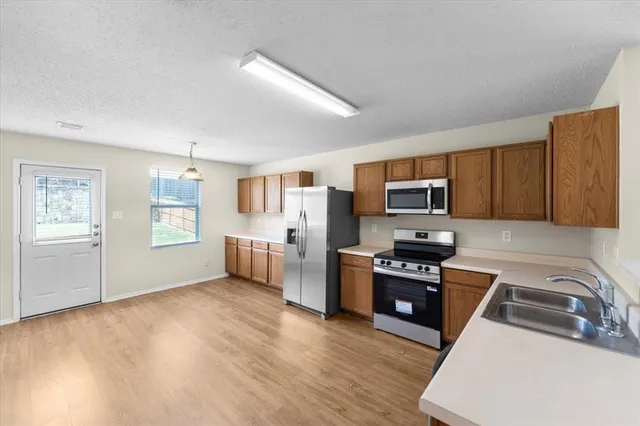 a kitchen with stainless steel appliances a stove a sink a refrigerator white cabinets and wooden floor